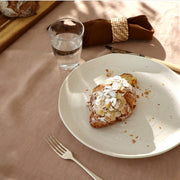 A beautifully set table featuring a croissant on a plate and a Linen Napkins Set 2 Tobacco elegantly displayed.