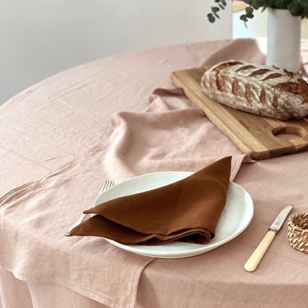 Linen Table Runners Blush elegantly set on a dining table with a plate, napkin, and rustic bread for a stylish decor.