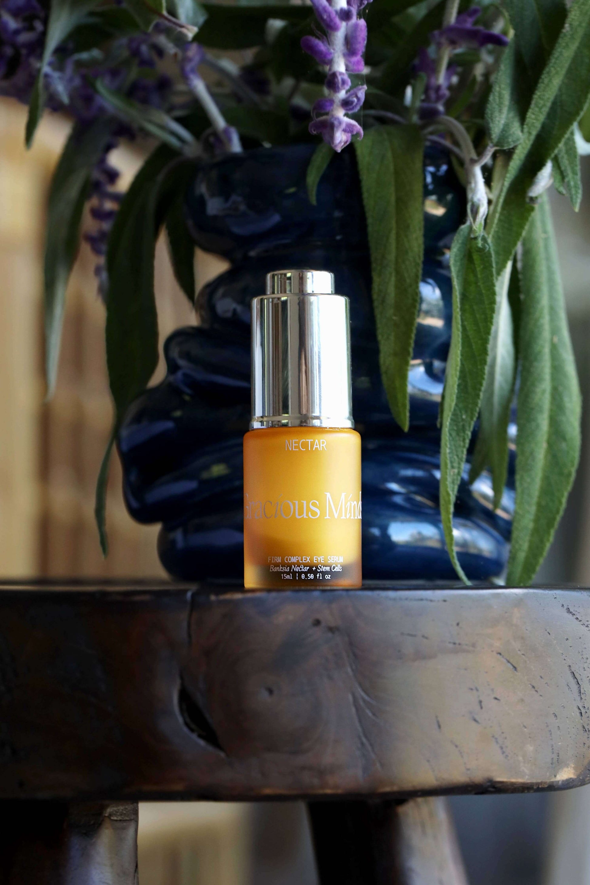 Gracious Minds Nectar Firming Eye Serum Elixir 15ml bottle with floral background, promoting hydrated and smooth skin around the eyes.