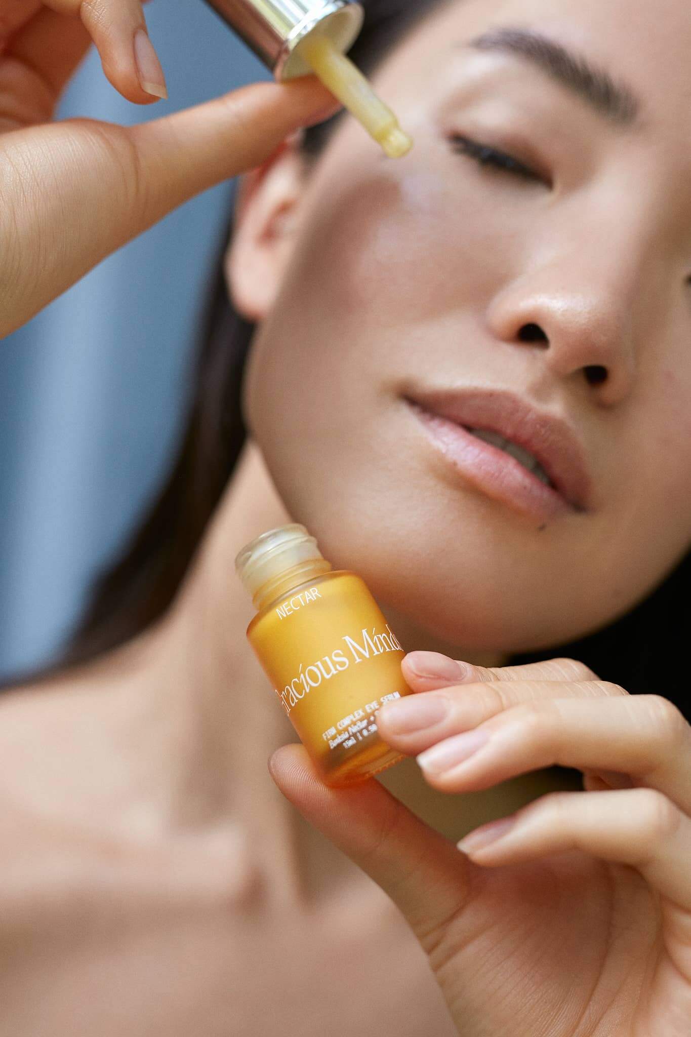 Woman applying Gracious Minds Nectar Firming Eye Serum Elixir 15ml to her eye area for hydration and smoothing.