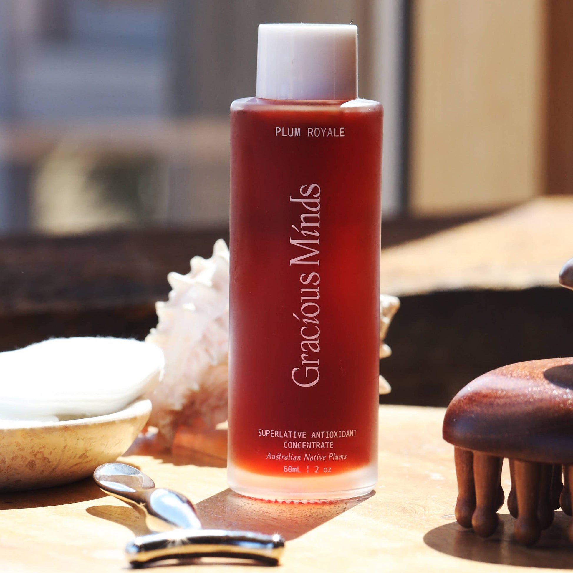 Gracious Minds Plum Royale Superlative Antioxidant Concentrate bottle on a wooden surface with skincare tools.
