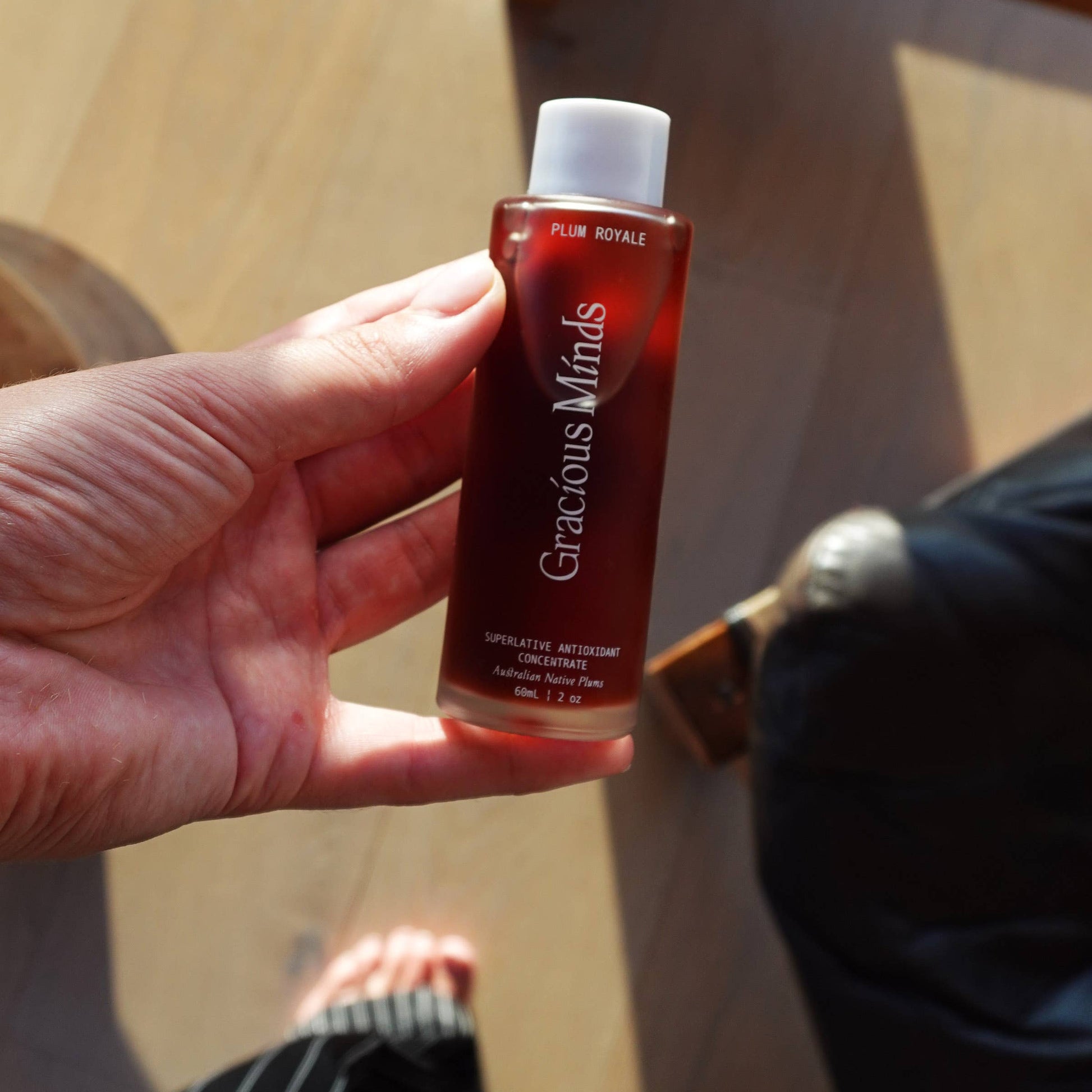Hand holding Gracious Minds Plum Royale Superlative Antioxidant Concentrate bottle indoors