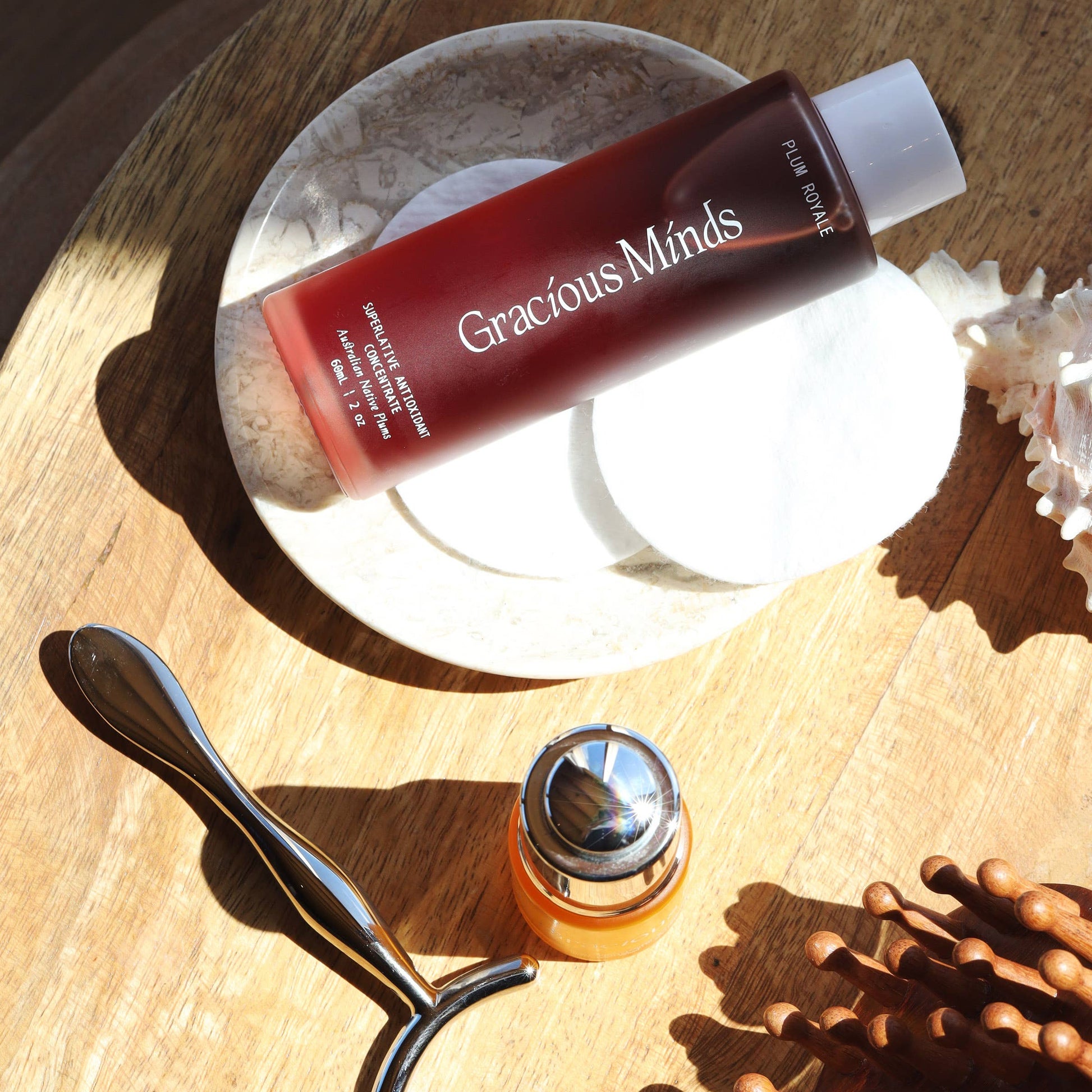 Gracious Minds Plum Royale Superlative Antioxidant Concentrate bottle displayed with skincare tools for facial treatment.