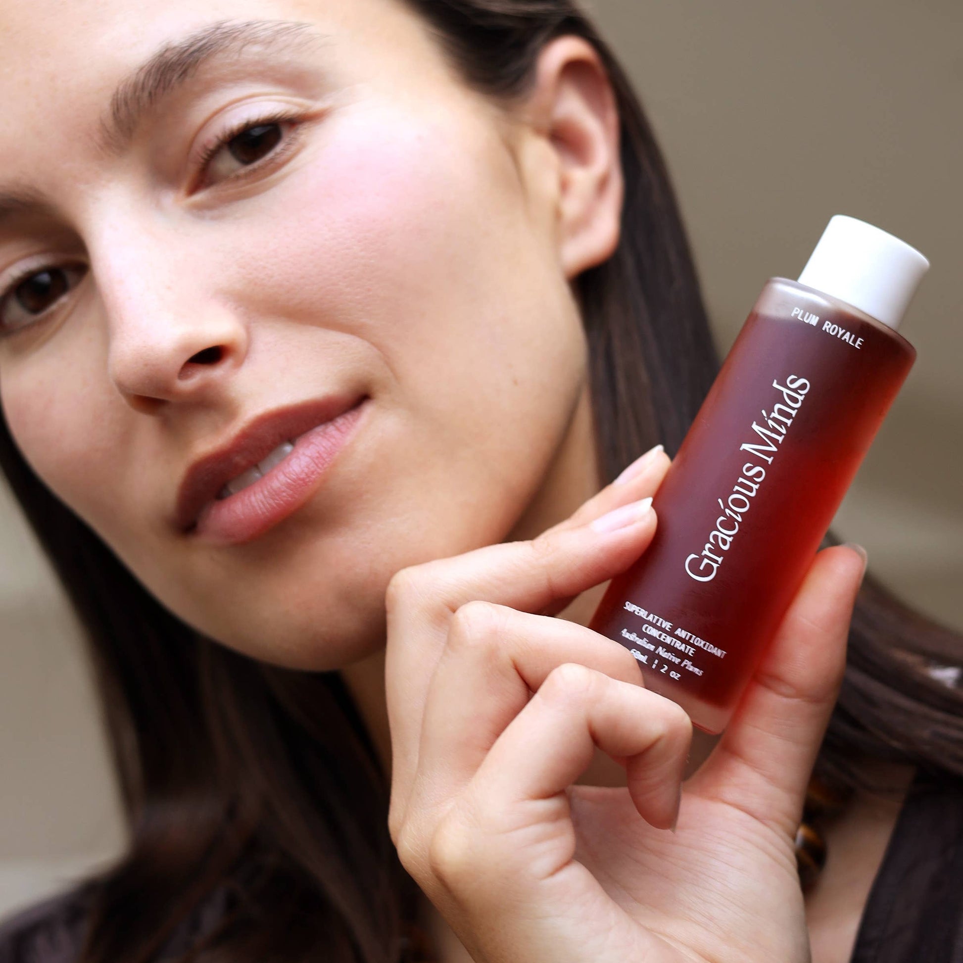 Woman holding a bottle of Gracious Minds Plum Royale Superlative Antioxidant Concentrate for facial treatment.