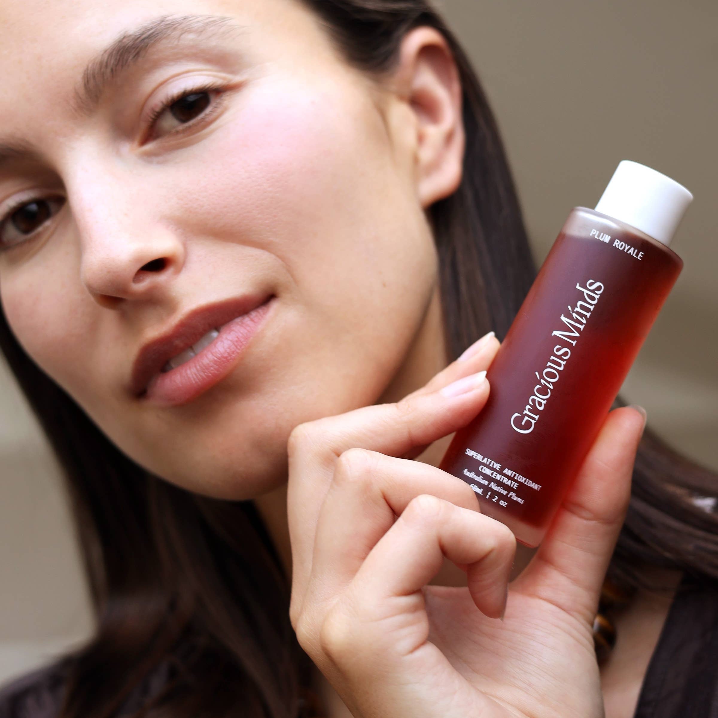 Woman holding a bottle of Gracious Minds Plum Royale Superlative Antioxidant Concentrate for facial treatment.