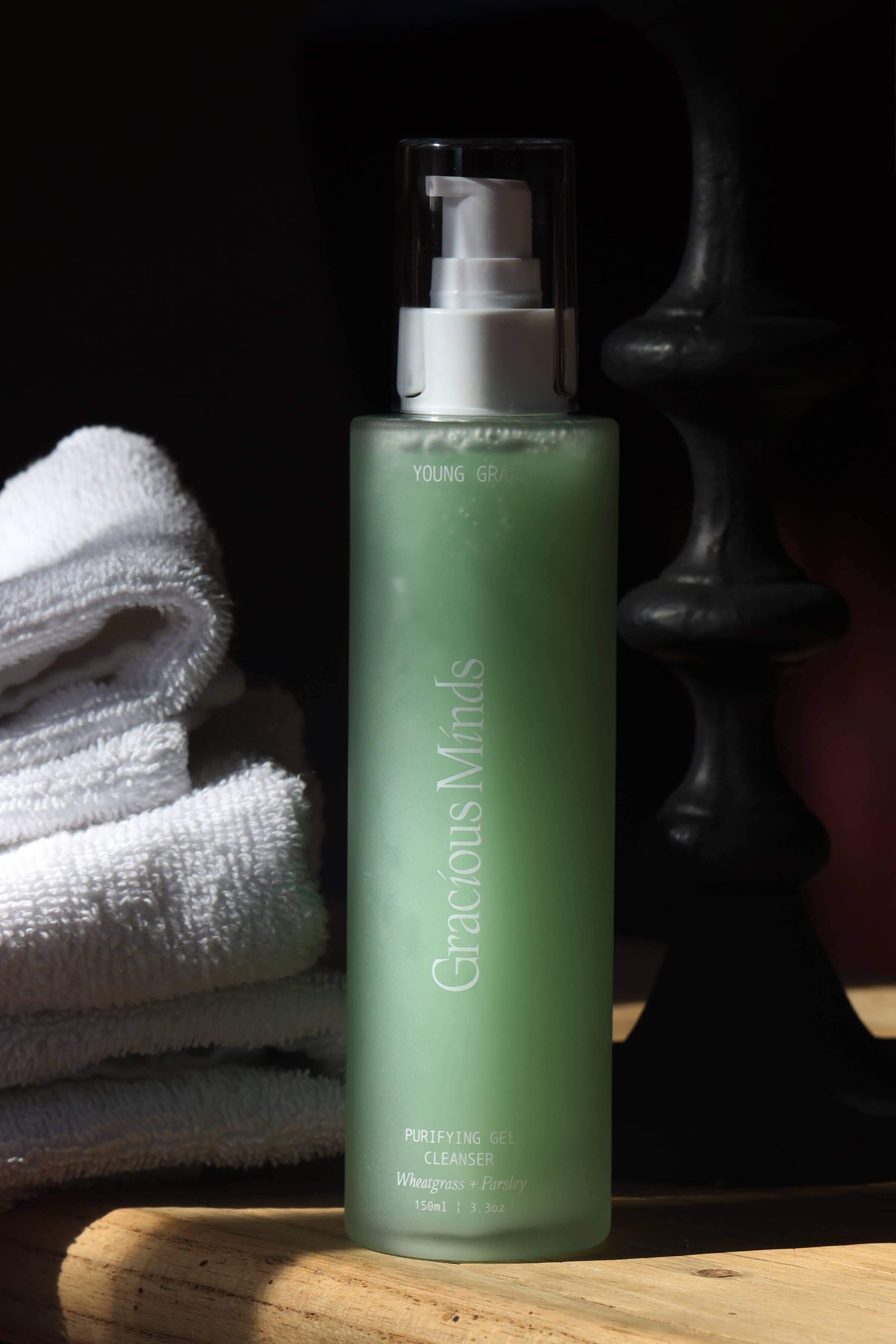 Gracious Minds Young Grass Purifying Gel Cleanser 150ml bottle next to towels, ideal for gentle daily face cleansing.