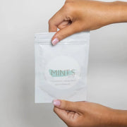 Hand holding a package of Mint.s Face Scrub, a gentle exfoliating skin care product.