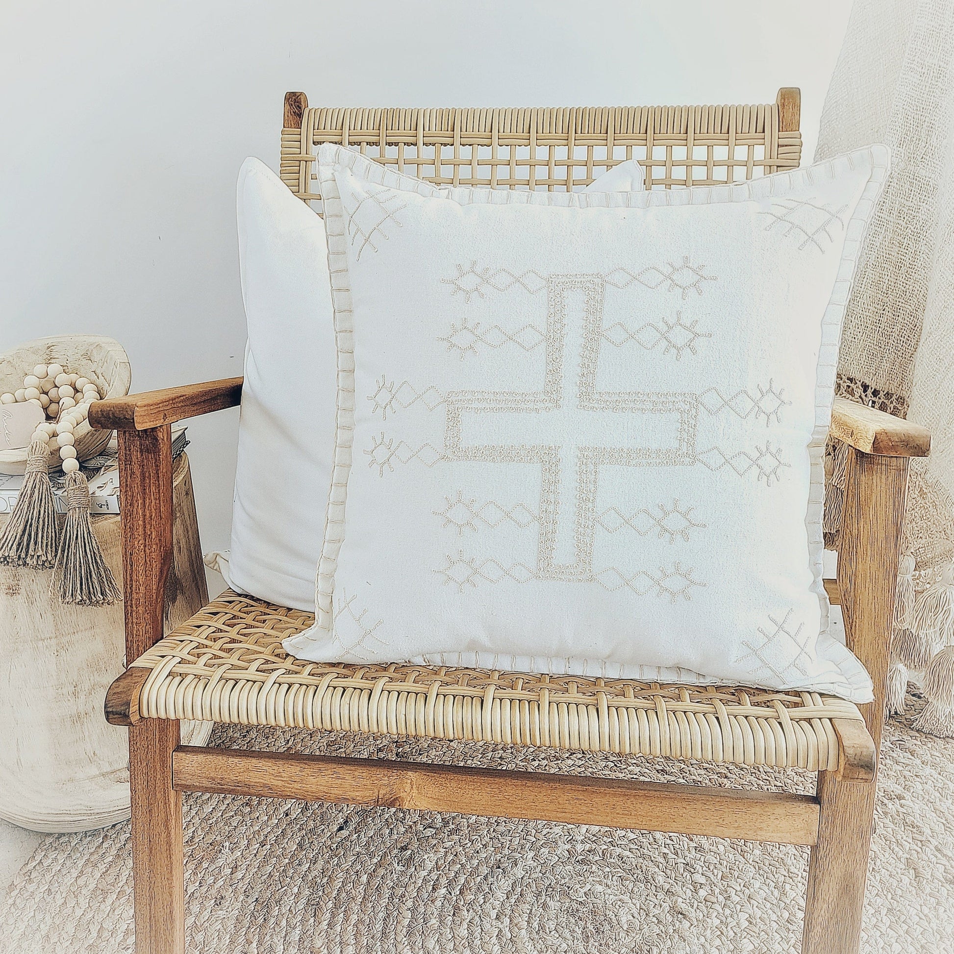 Boho Cross Cushion Natural on a rattan chair, featuring a stitched cross pattern and natural fabric texture.