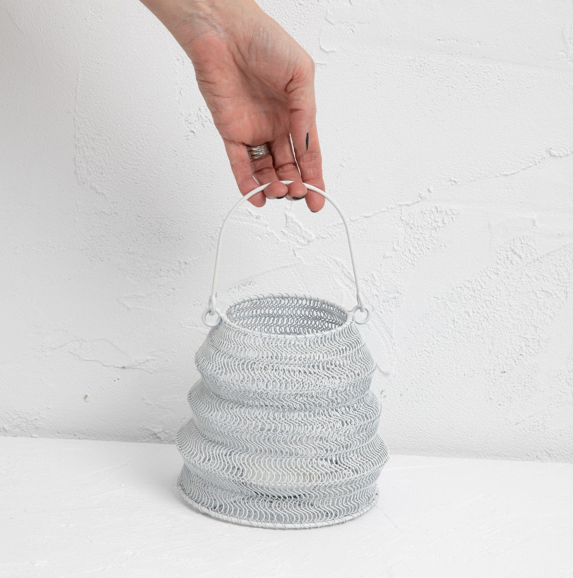 Mesh Lanterns White decorative iron lantern held by a hand against a textured background.