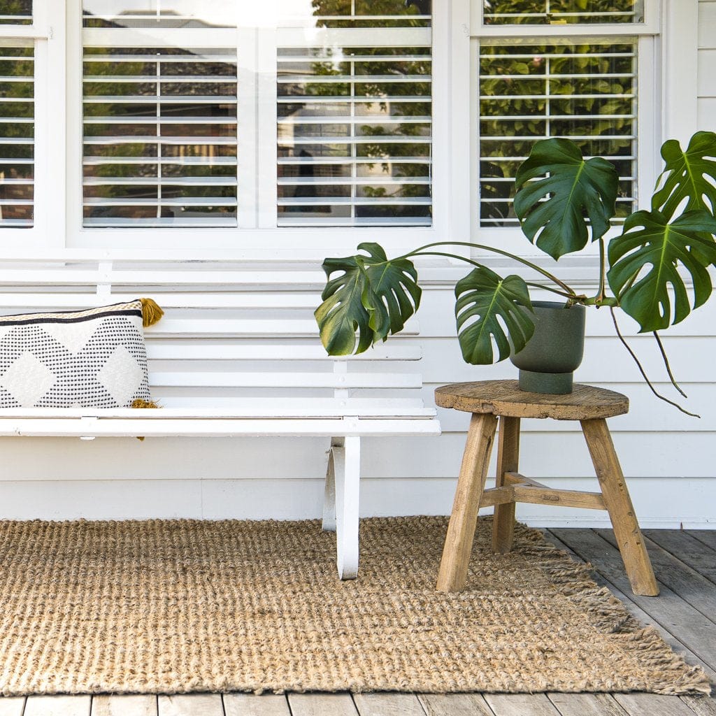 Natural Jute Rugs Fringe Edge placed under a white bench, enhancing outdoor decor with texture and warmth.
