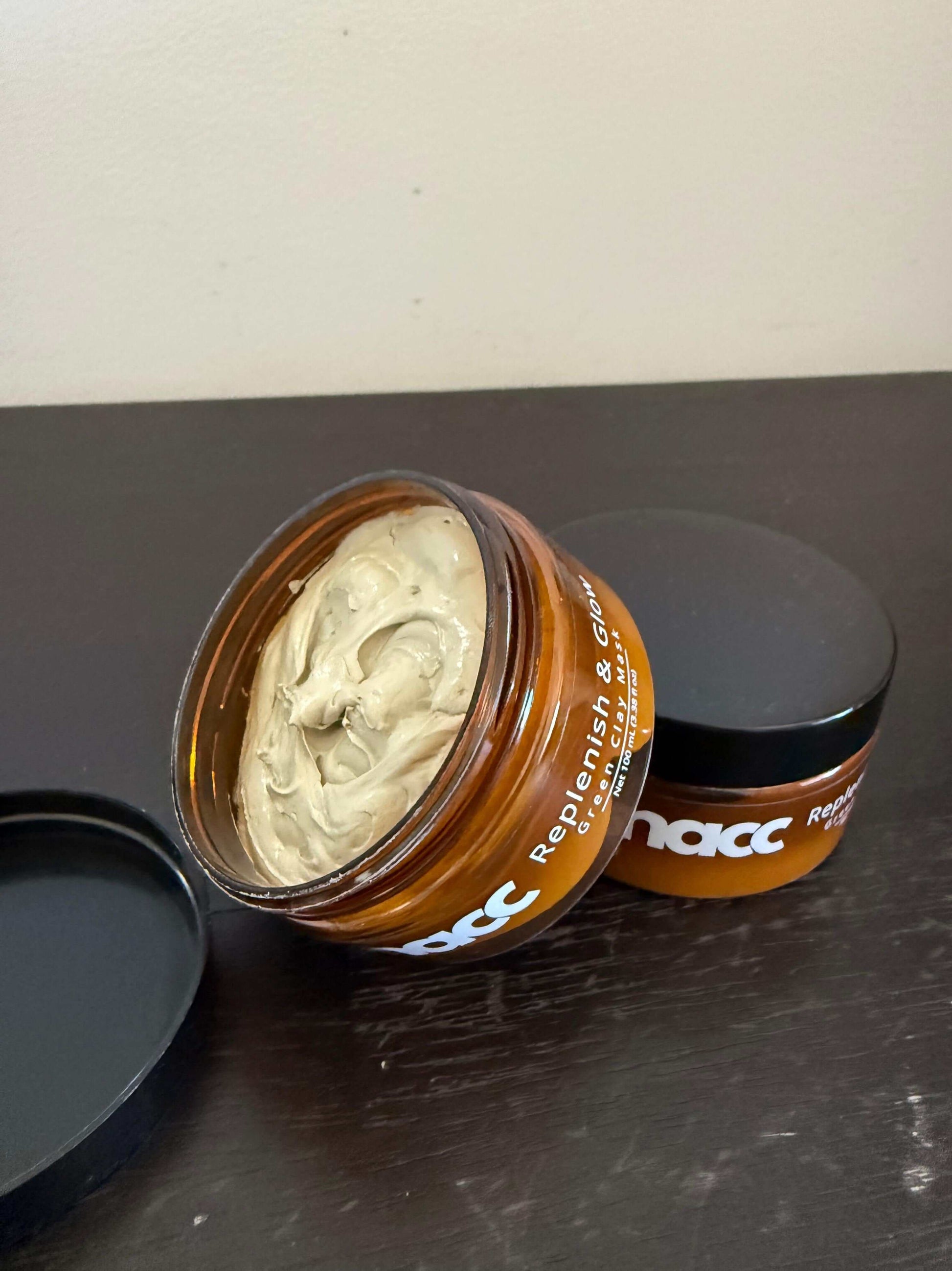 Open jar of SNACC Beauty Replenish & Glow Green Clay Face Mask on a dark surface