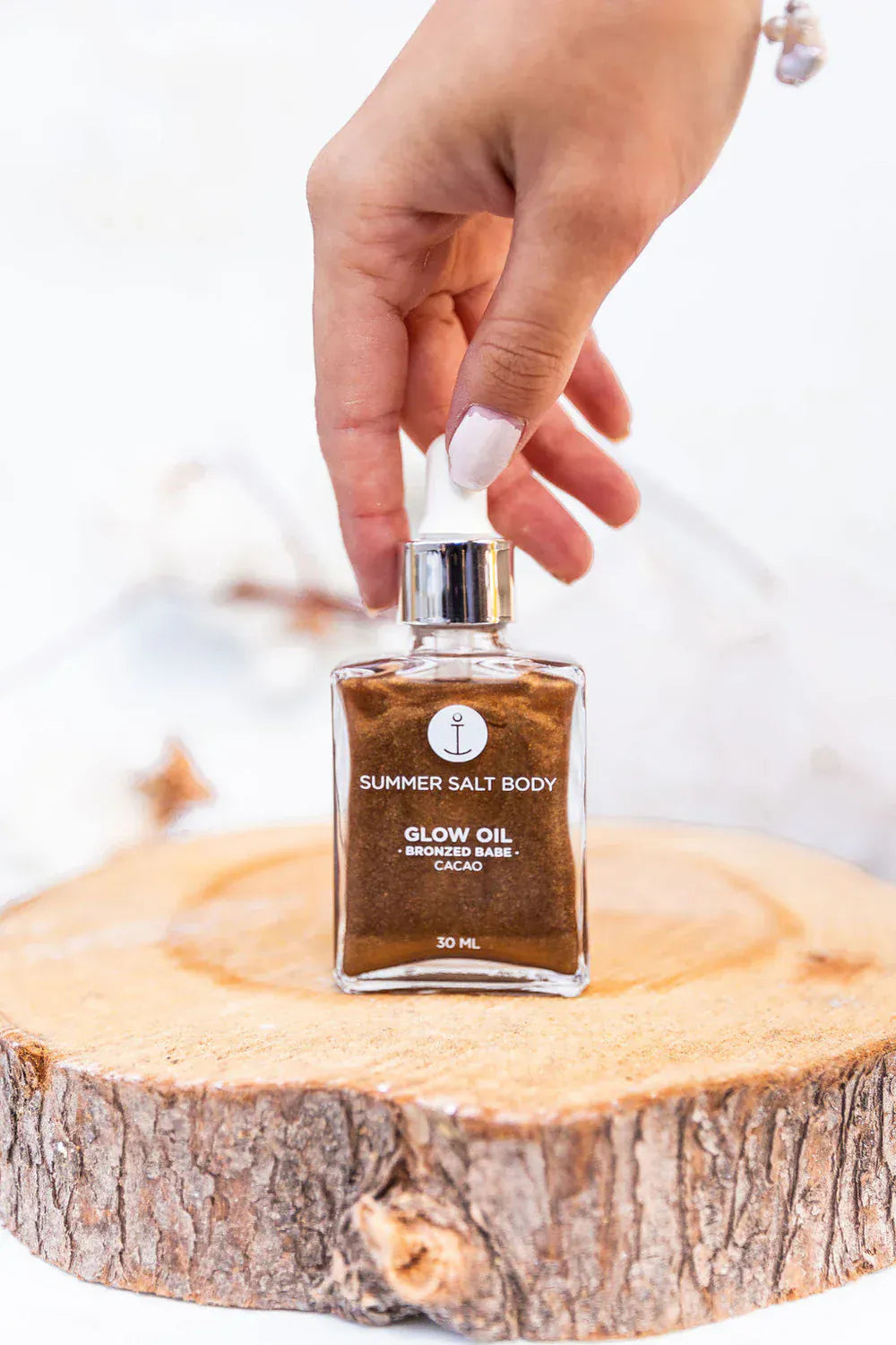 Hand holding Summer Salt Body Bronzed Babe Glow Oil 100ml on a wooden surface