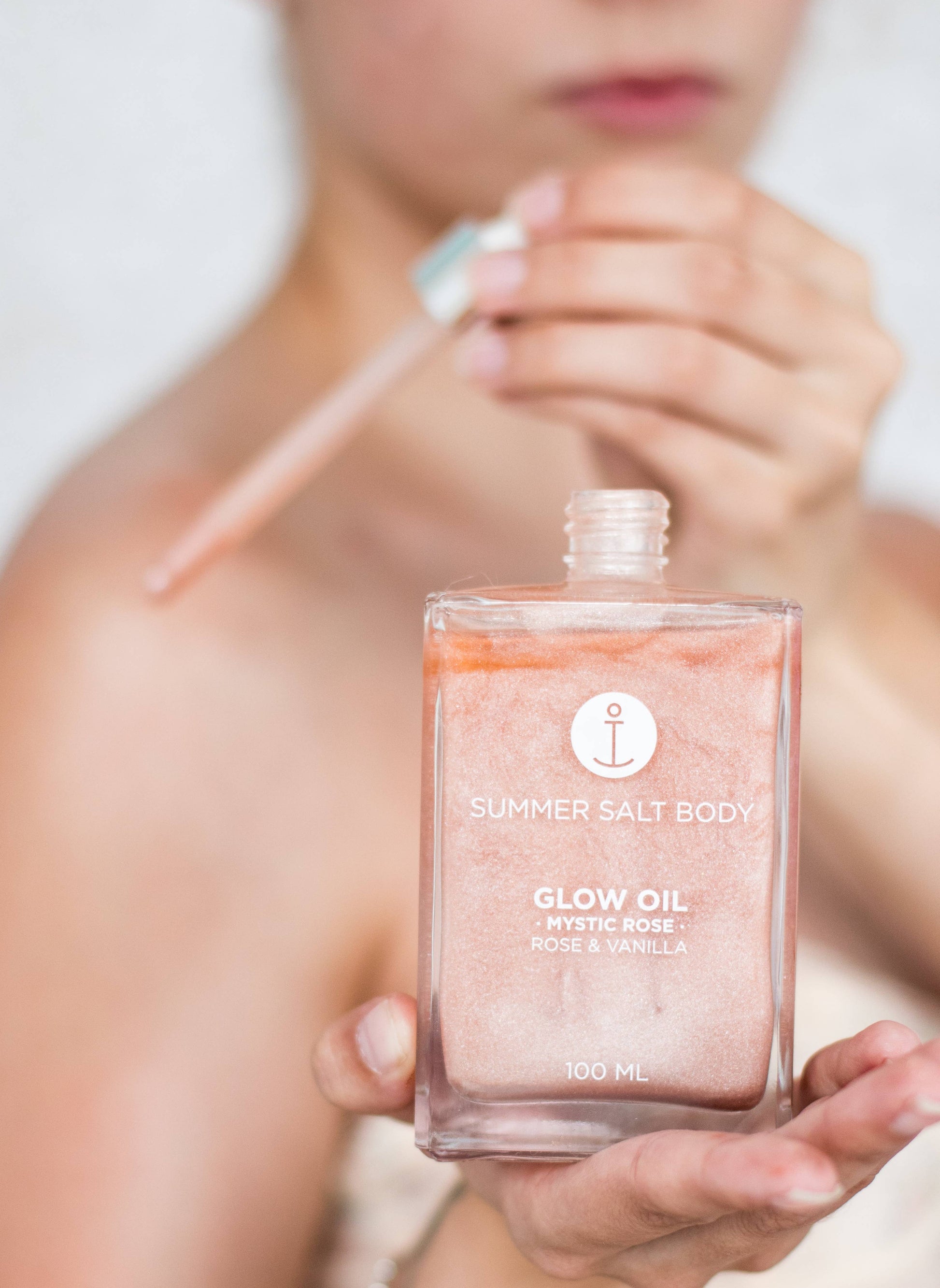Woman holding Summer Salt Body Mystic Rose Body Glow Oil 100ml bottle, showcasing luxurious hydrating glow oil.