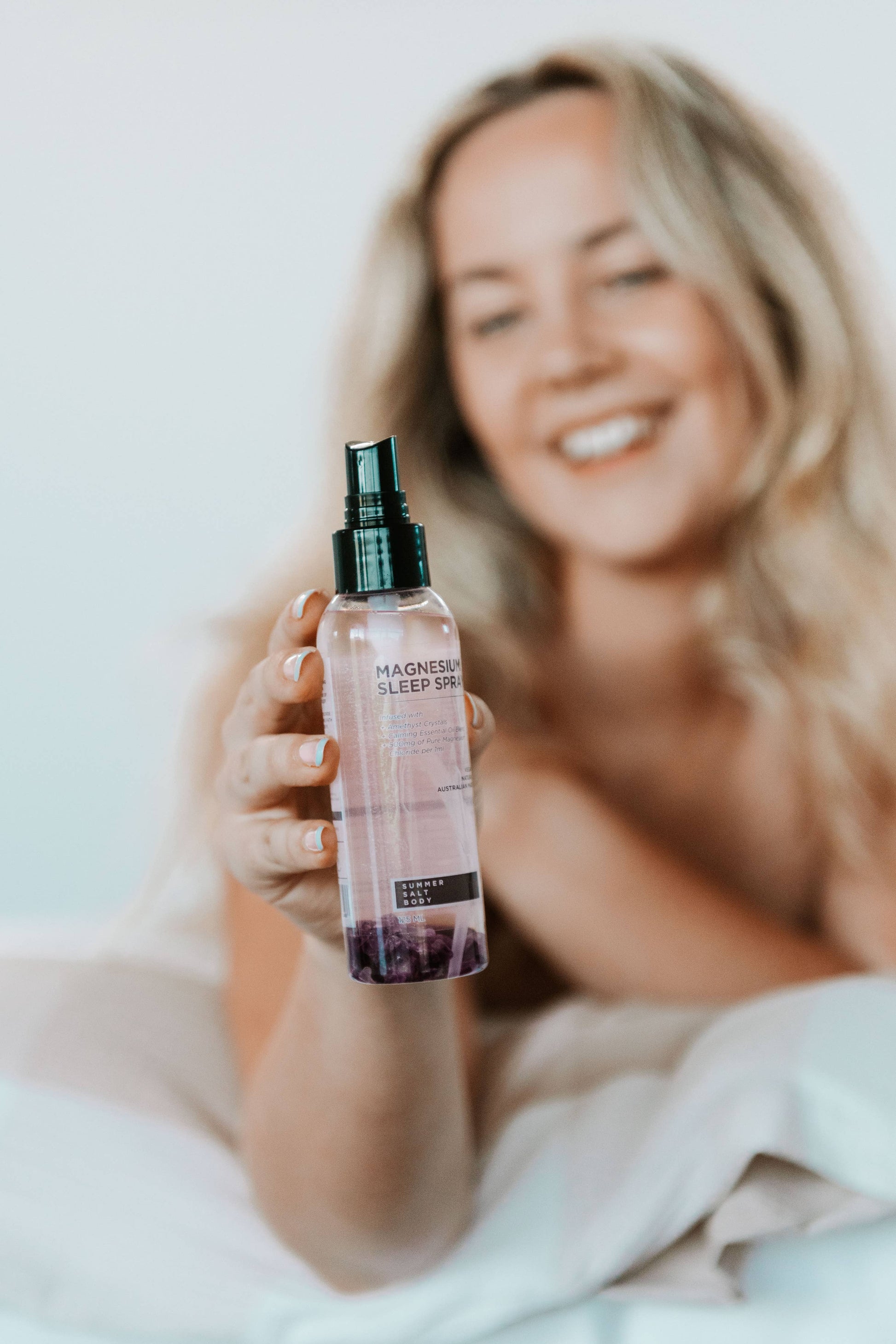 Woman holding Summer Salt Body Magnesium Sleep Spray with amethyst, promoting relaxation and restful sleep, 125ml bottle.