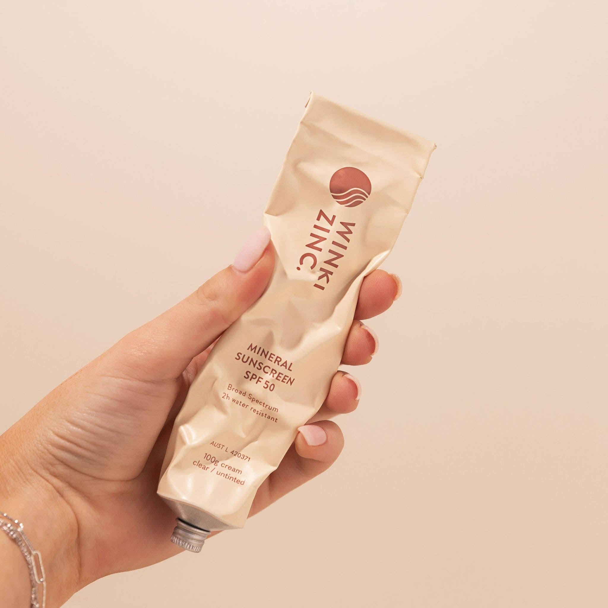 Hand holding Winki Zinc Natural Mineral Sunscreen SPF 50 tube in a beige background