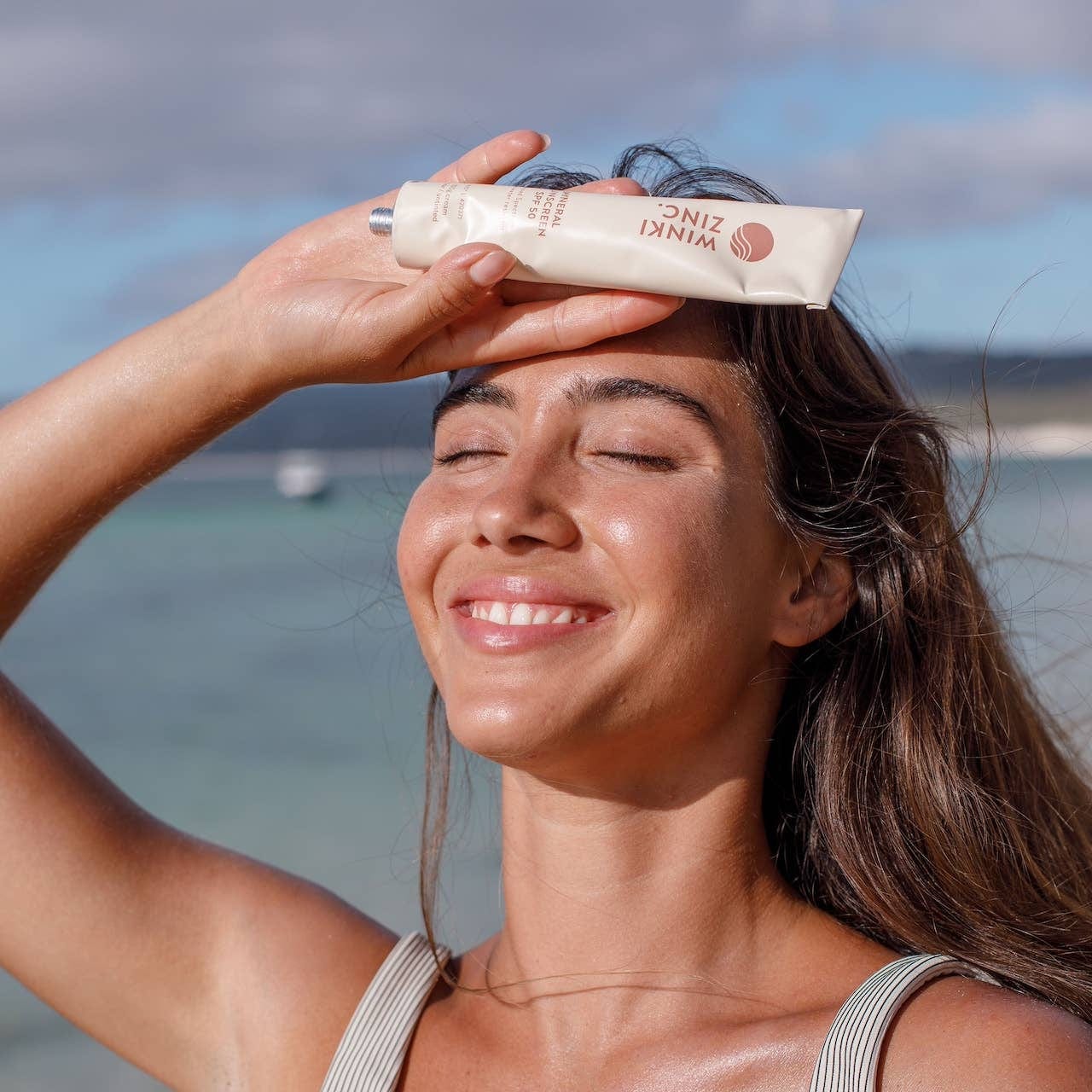 Woman applying Winki Zinc Natural Mineral Sunscreen SPF 50 at the beach